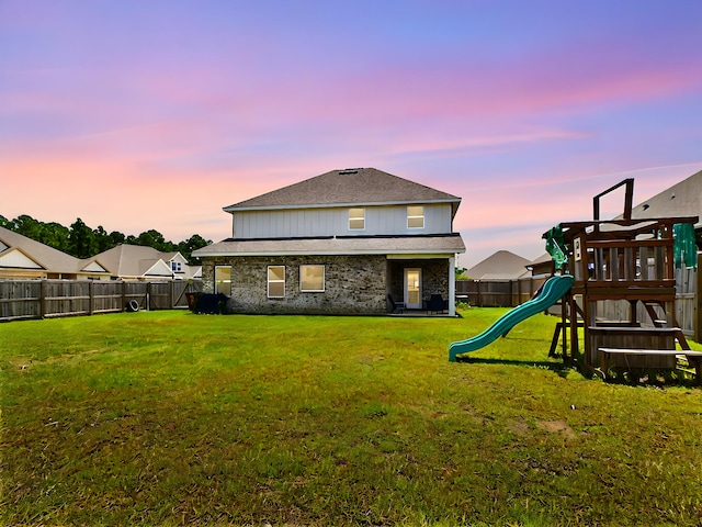 back house at dusk featuring a playground and a yard