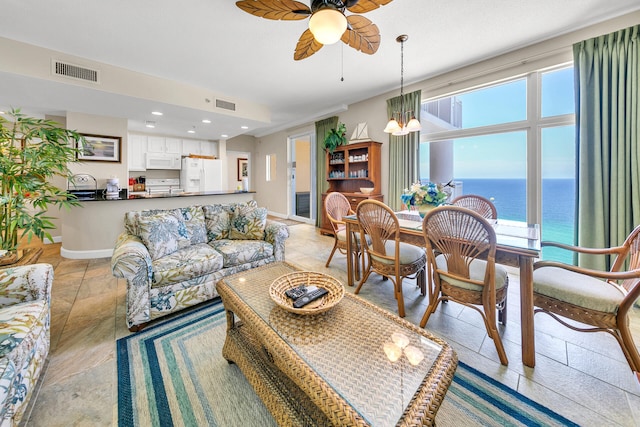 living room with ceiling fan with notable chandelier, a water view, and a healthy amount of sunlight