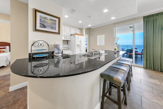 kitchen featuring a kitchen bar, white appliances, a healthy amount of sunlight, sink, and white cabinets