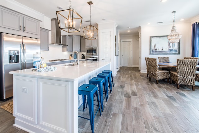 kitchen with light countertops, gray cabinetry, appliances with stainless steel finishes, a sink, and wall chimney range hood