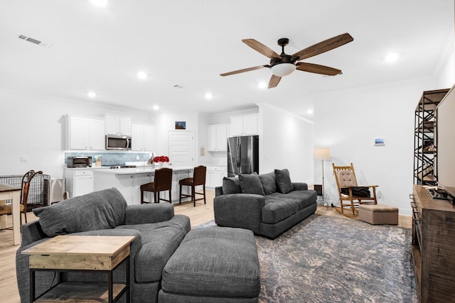 living room with light hardwood / wood-style floors, ceiling fan, and ornamental molding