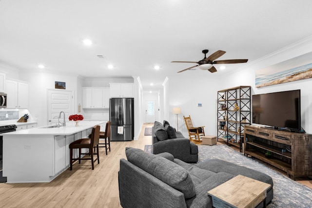 living room featuring light wood-type flooring, ceiling fan, ornamental molding, and sink