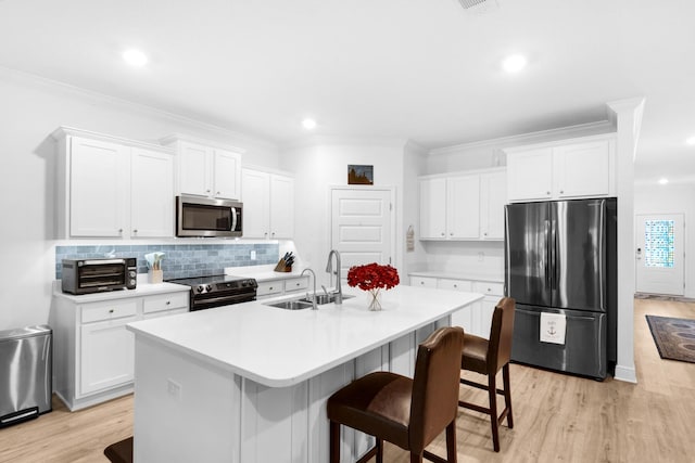 kitchen with appliances with stainless steel finishes, a breakfast bar, sink, a center island with sink, and white cabinets