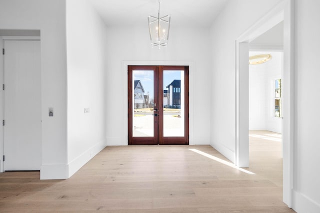 foyer entrance with a notable chandelier, light wood-type flooring, and french doors