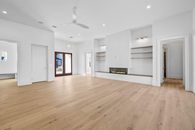 unfurnished living room featuring a large fireplace, ceiling fan with notable chandelier, and light hardwood / wood-style floors