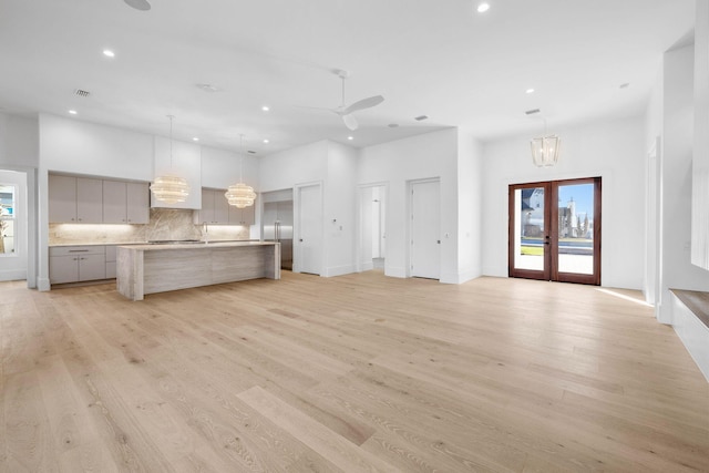 unfurnished living room featuring french doors, ceiling fan with notable chandelier, and light wood-type flooring