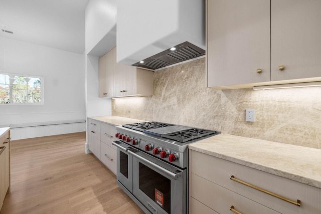 kitchen featuring decorative backsplash, premium range hood, light stone counters, double oven range, and light hardwood / wood-style floors