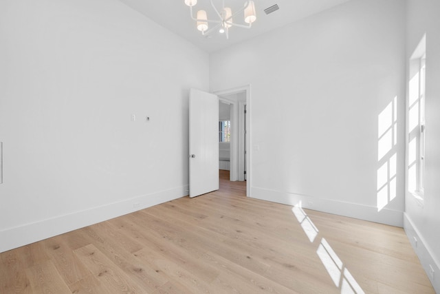 spare room featuring a chandelier, a towering ceiling, and light hardwood / wood-style floors