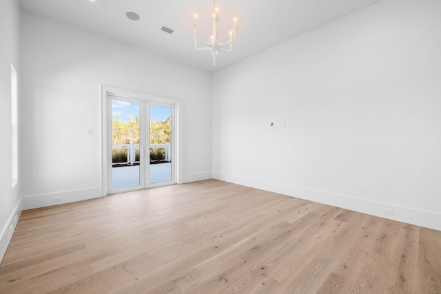 spare room featuring light wood-type flooring and an inviting chandelier