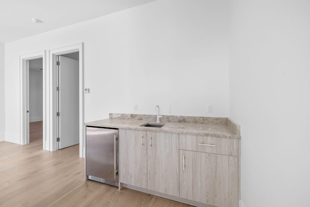 bar with light brown cabinetry, stainless steel refrigerator, sink, and light hardwood / wood-style floors