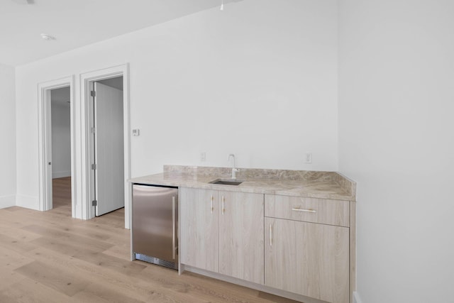 bar featuring light brown cabinetry, stainless steel fridge, sink, and light hardwood / wood-style flooring