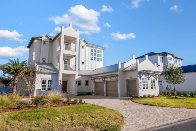 view of front facade with decorative driveway, an attached garage, a standing seam roof, metal roof, and a front lawn