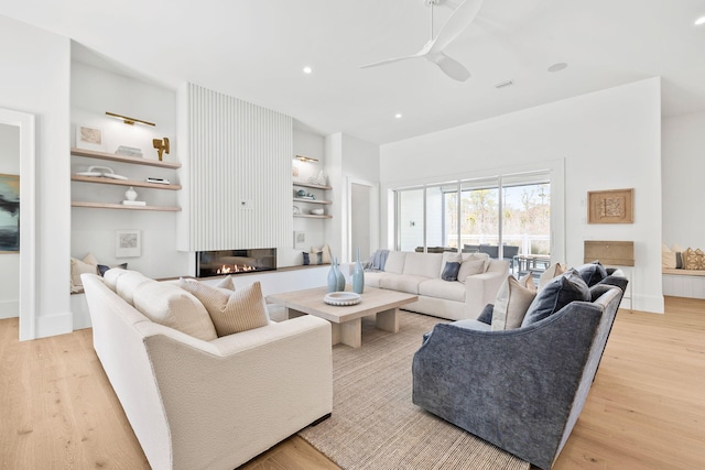 living room with light wood-style floors, a glass covered fireplace, recessed lighting, and a ceiling fan