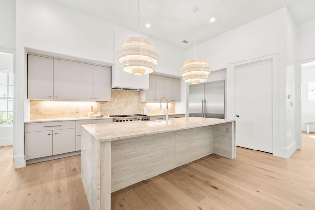 kitchen with a towering ceiling, a sink, light wood-type flooring, range, and built in refrigerator