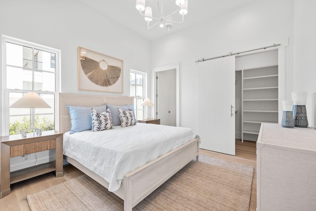 bedroom featuring light wood-type flooring, a barn door, a spacious closet, and a chandelier