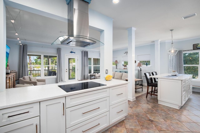 kitchen featuring black electric stovetop, ornate columns, island range hood, pendant lighting, and white cabinetry