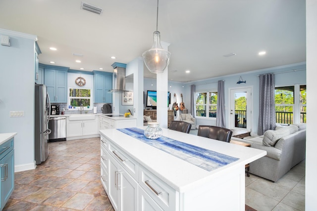 kitchen featuring wall chimney range hood, sink, ornamental molding, blue cabinetry, and a kitchen island