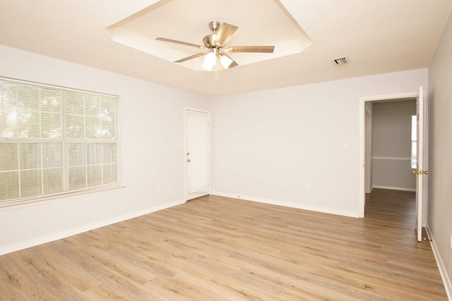 spare room with ceiling fan, a raised ceiling, and light wood-type flooring