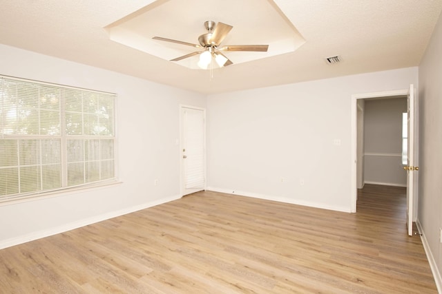 empty room featuring ceiling fan, a tray ceiling, and light wood-type flooring