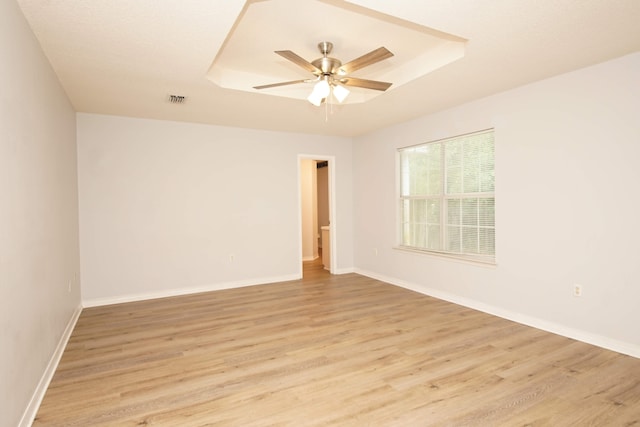 empty room featuring ceiling fan, light wood-type flooring, and a raised ceiling