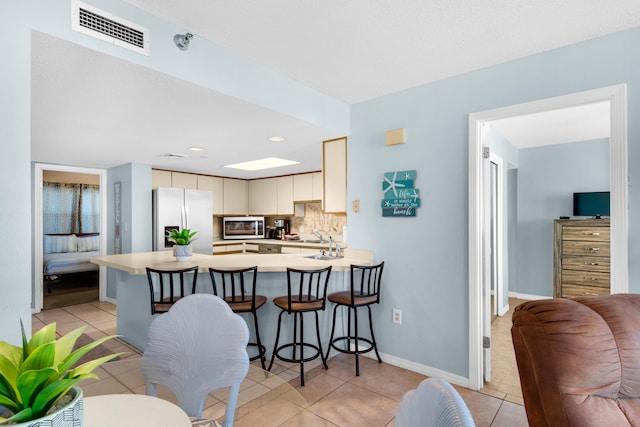 kitchen with light tile patterned flooring, backsplash, kitchen peninsula, stainless steel appliances, and cream cabinets