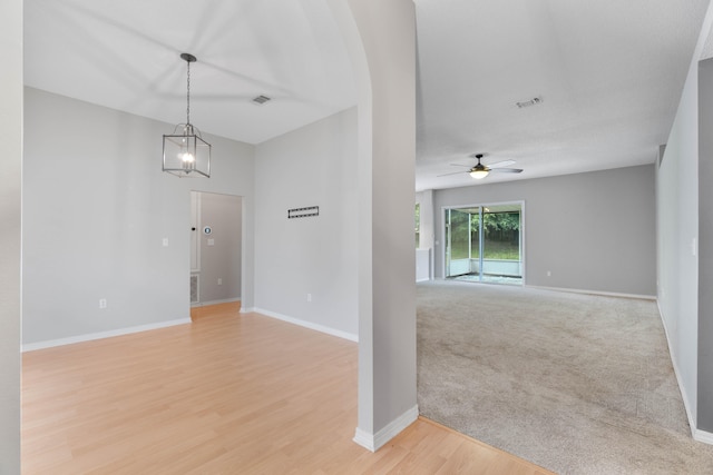 carpeted spare room with ceiling fan with notable chandelier