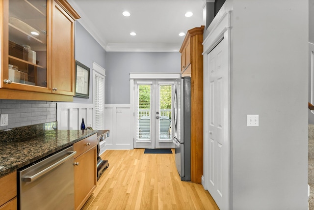 kitchen with appliances with stainless steel finishes, backsplash, crown molding, light hardwood / wood-style flooring, and dark stone countertops