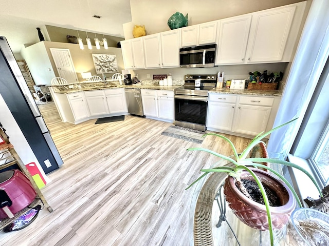 kitchen featuring kitchen peninsula, stainless steel appliances, light stone counters, and white cabinetry