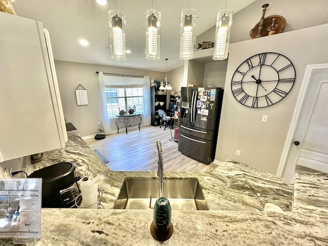 kitchen with sink, a textured ceiling, lofted ceiling, black refrigerator with ice dispenser, and light hardwood / wood-style flooring