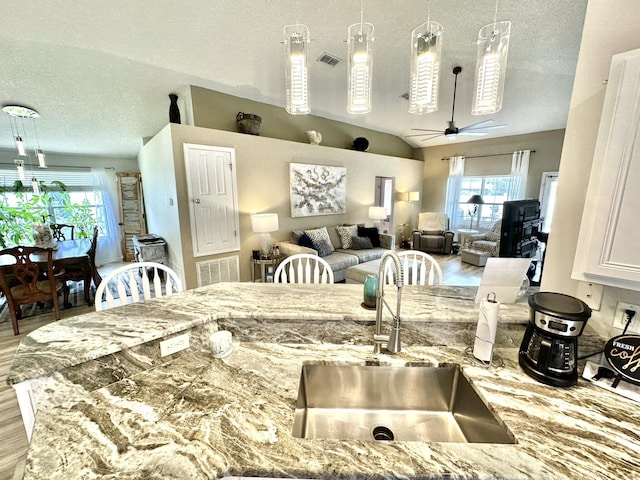 kitchen with light stone counters, vaulted ceiling, decorative light fixtures, ceiling fan, and sink