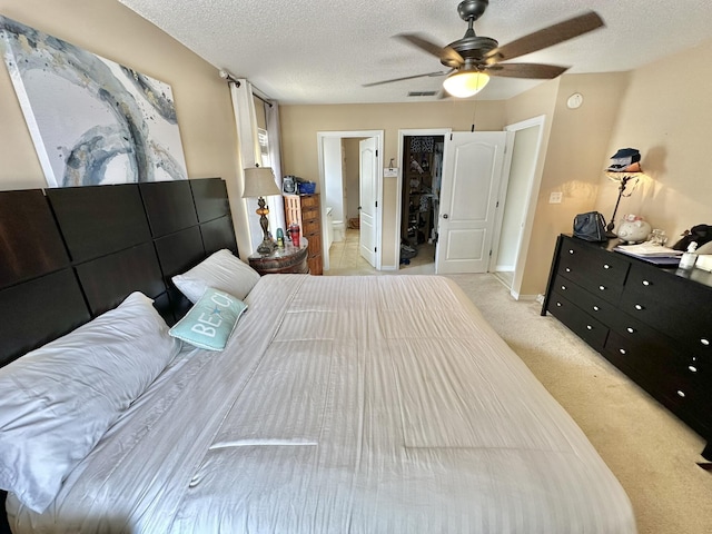 bedroom with a textured ceiling, a spacious closet, a closet, light colored carpet, and ceiling fan