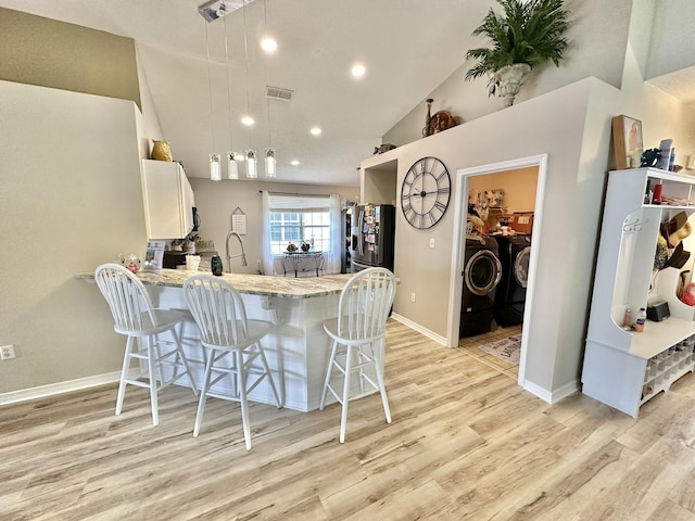 kitchen with separate washer and dryer, kitchen peninsula, a breakfast bar area, stainless steel refrigerator with ice dispenser, and pendant lighting