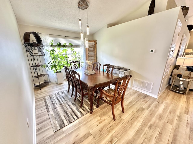 dining room with lofted ceiling, a textured ceiling, and light hardwood / wood-style flooring