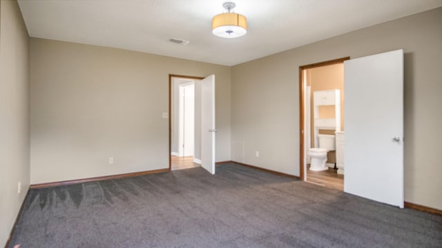 unfurnished bedroom featuring dark carpet and connected bathroom