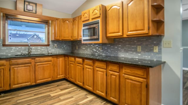 kitchen featuring stainless steel microwave, light wood-type flooring, lofted ceiling, dark stone countertops, and sink