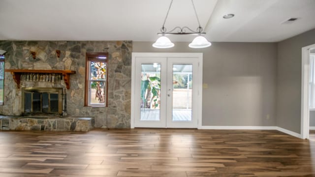 unfurnished living room with dark hardwood / wood-style flooring, a stone fireplace, and french doors