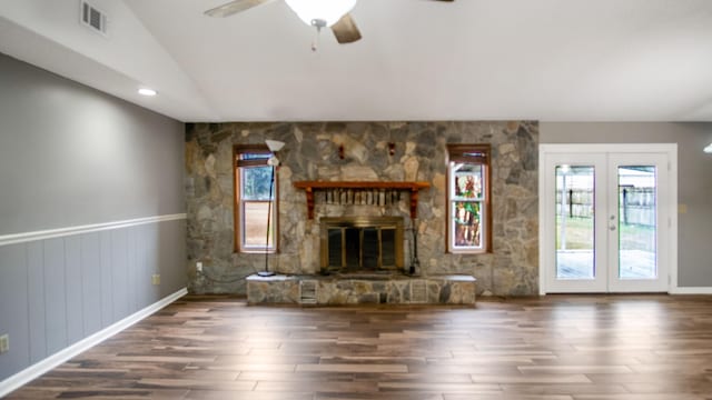 unfurnished living room featuring ceiling fan, vaulted ceiling, dark hardwood / wood-style floors, a stone fireplace, and french doors