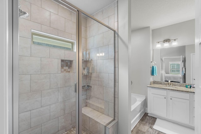 bathroom with plus walk in shower, vanity, a textured ceiling, and hardwood / wood-style flooring