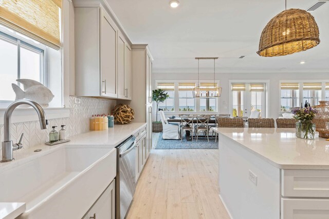 kitchen featuring a wealth of natural light, light hardwood / wood-style flooring, stainless steel dishwasher, and pendant lighting