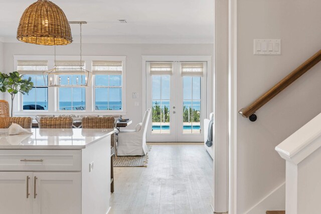 interior space with light hardwood / wood-style floors, french doors, light stone counters, hanging light fixtures, and white cabinetry