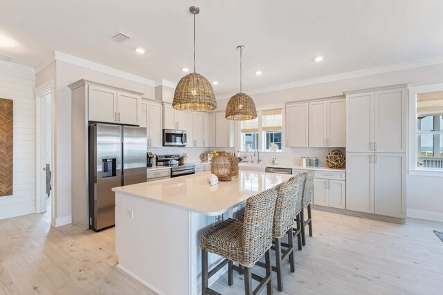 kitchen with light hardwood / wood-style floors, stainless steel appliances, backsplash, a center island, and a healthy amount of sunlight