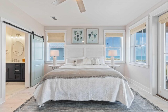 tiled bedroom with sink, a barn door, ceiling fan, and ensuite bath