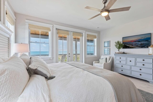 bedroom with a water view, light hardwood / wood-style floors, access to exterior, ceiling fan, and french doors