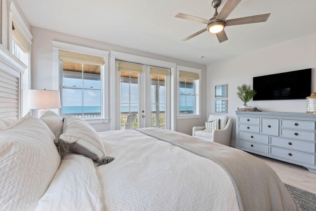 bedroom with a water view, light hardwood / wood-style floors, access to outside, ceiling fan, and french doors