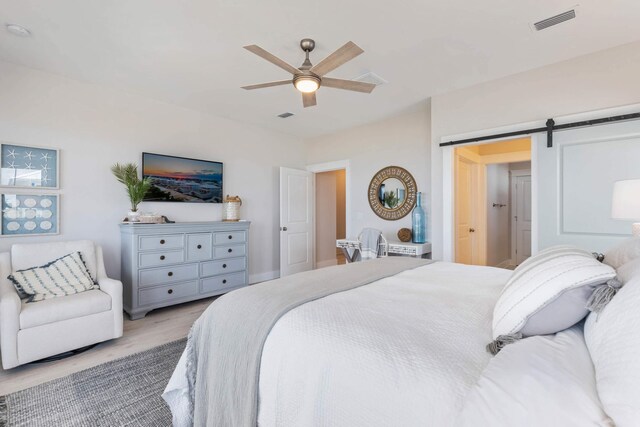 bedroom with a barn door, light hardwood / wood-style floors, and ceiling fan