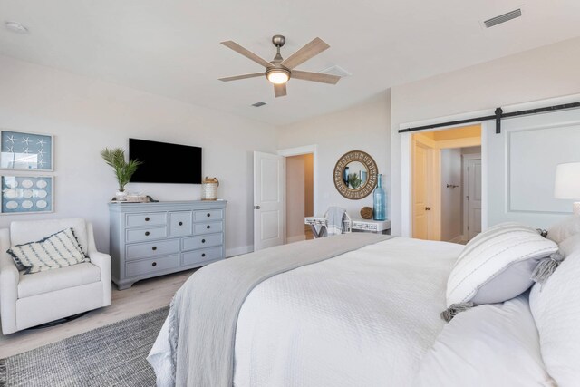 bedroom featuring a barn door, ceiling fan, and light hardwood / wood-style flooring