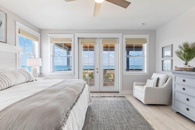 bedroom featuring access to outside, light hardwood / wood-style floors, multiple windows, and a water view