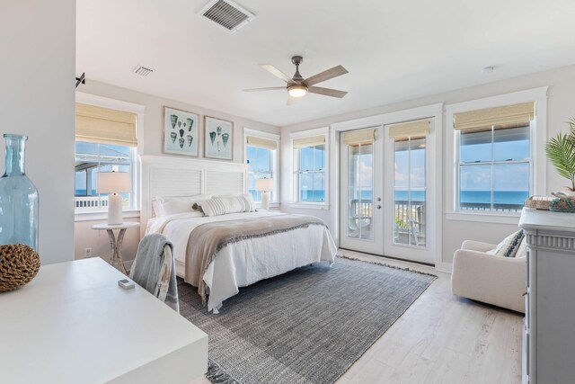 bedroom with french doors, light hardwood / wood-style flooring, access to outside, a water view, and ceiling fan