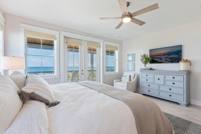 bedroom with light hardwood / wood-style floors, french doors, access to outside, a water view, and ceiling fan