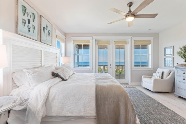 bedroom with french doors, light hardwood / wood-style flooring, access to outside, a water view, and ceiling fan